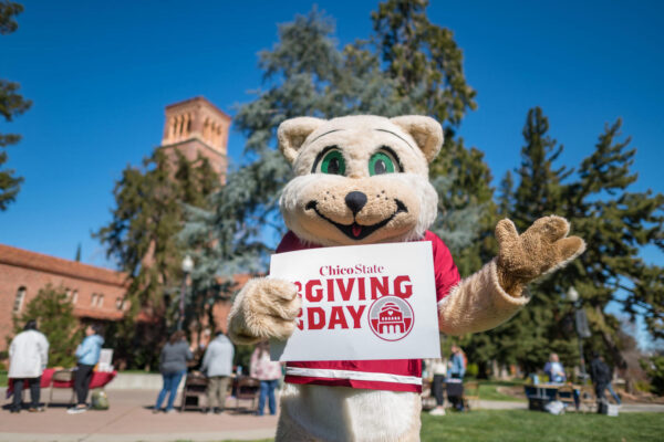 The Chico State mascot, "Willie," holds a Giving Day sign and waves to the camera.