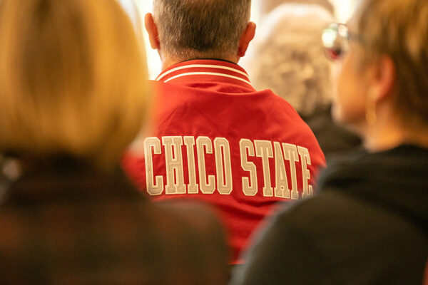 President's Perez sits with his back to the camera, wearing a red jacket with 'Chico State' written in bold white letters.