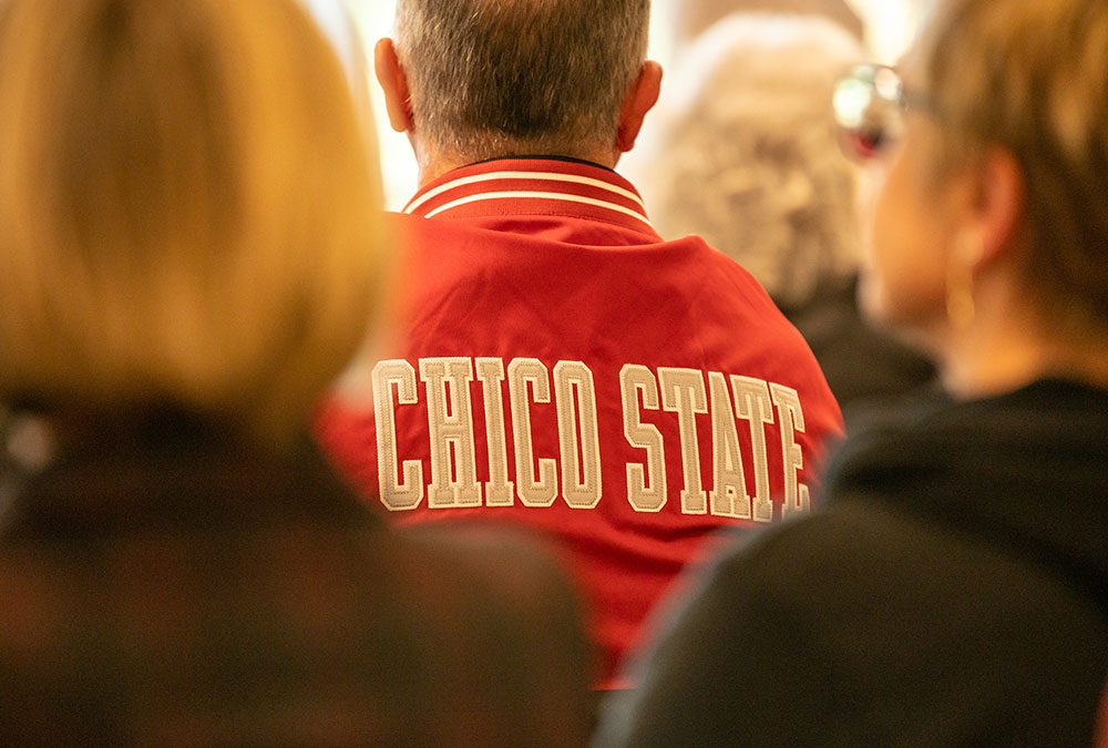 President's Perez sits with his back to the camera, wearing a red jacket with 'Chico State' written in bold white letters.