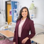 Claudia Ruiz wears a two-piece burgundy suit and pink blouse as she is photographed in the School of Nursing's state-of-the-art simulation center on campus.