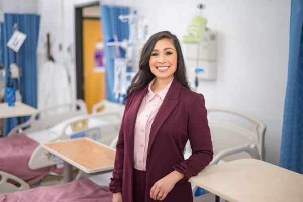 Claudia Ruiz wears a two-piece burgundy suit and pink blouse as she is photographed in the School of Nursing's state-of-the-art simulation center on campus.