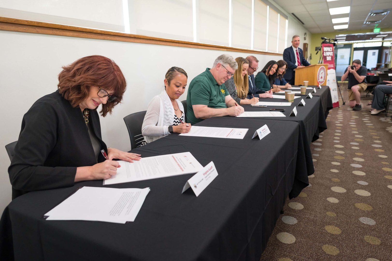Seven community college presidents sit in a row as they sign their MOUs.