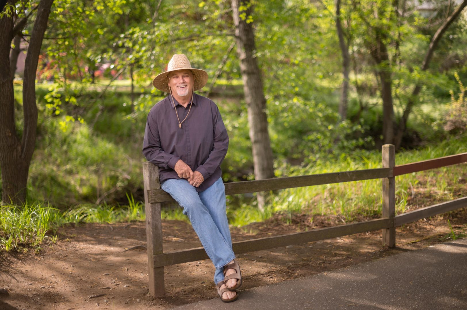 Mark Stemen wears a sun hat as he sits on a wooden fence.