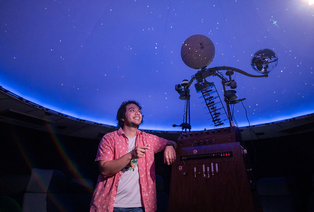 Giovanni Paz-Silva looks up at the ceiling inside Chico State's planetarium, using a laser pointer to identify a star. 