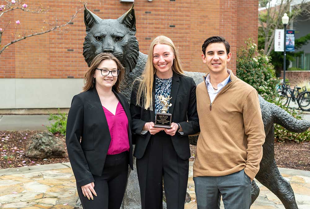 From left to right, Natalie Bourn, Kristen Chatham, and Finn Blacker pose in front of a Wildcat statue. Chatham holds a small trophy in her hand.