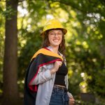 Olivia Wiemann poses in her master's gown and a yellow hard hat.