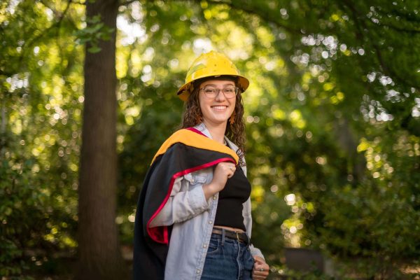 Olivia Wiemann poses in her master's gown and a yellow hard hat.