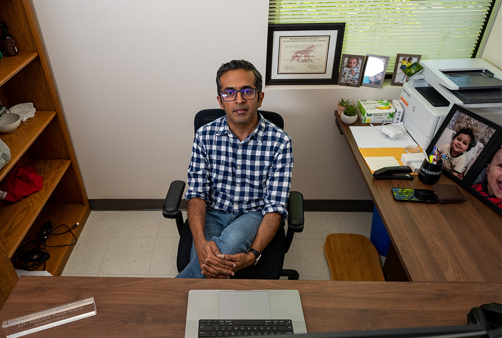 Professor Abbas Artawalla is seen from above, sitting at his desk in front of a laptop.