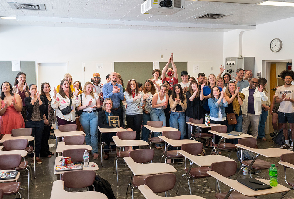 Lecturer Tess is surrounded by students, faculty, and University leadership in her classroom, during a surprise ceremony to honor her with an Outstanding Faculty Award. 