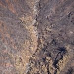 An aerial photo shows a muddy creek in a heavily scorched canyon.