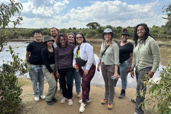 A group of people stand at the bank of a river to pose for a photo.