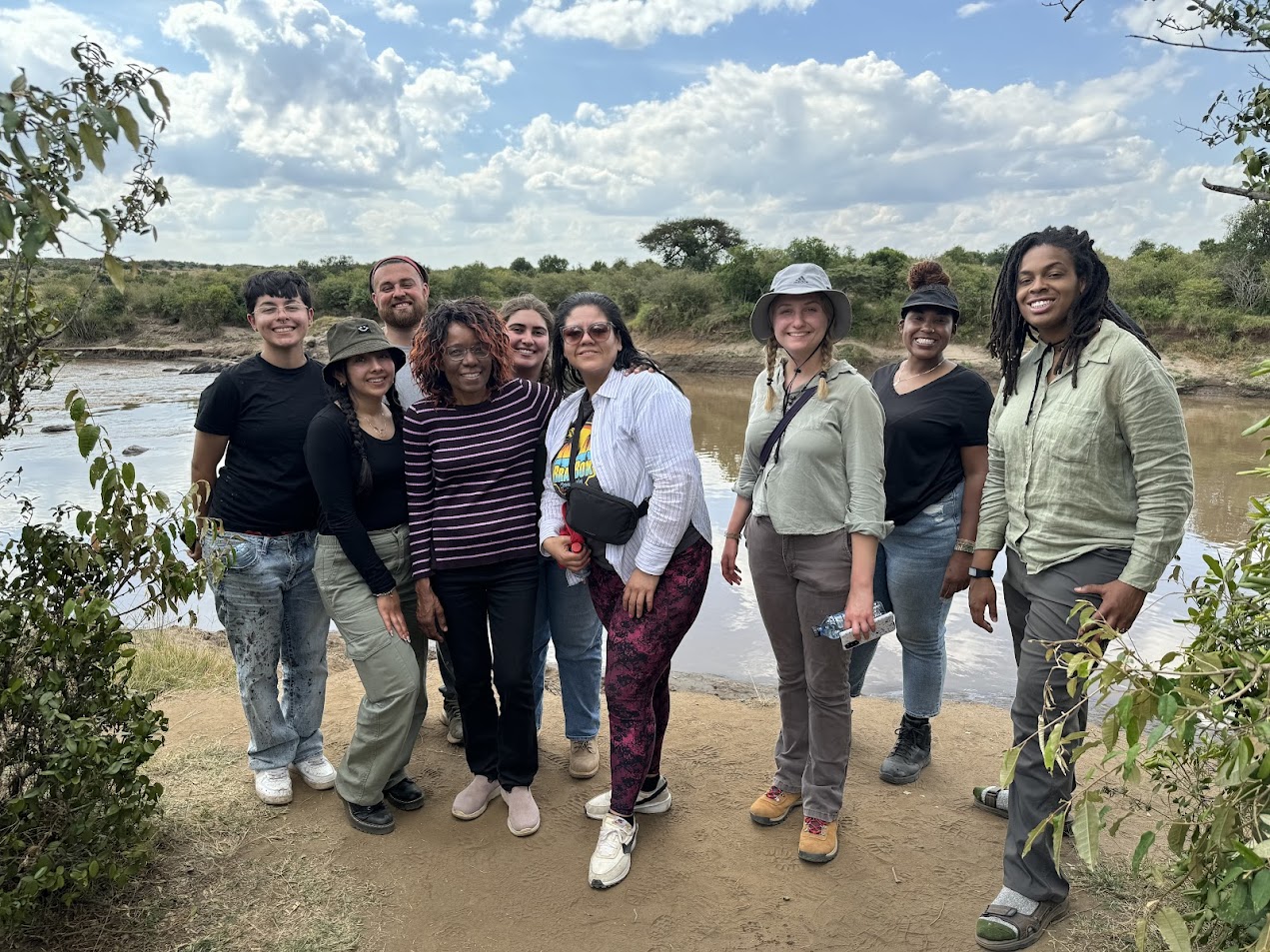 A group of people stand at the bank of a river to pose for a photo.