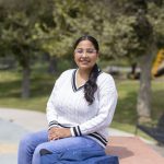 A woman poses for the camera while sitting on an outside bench at a park.