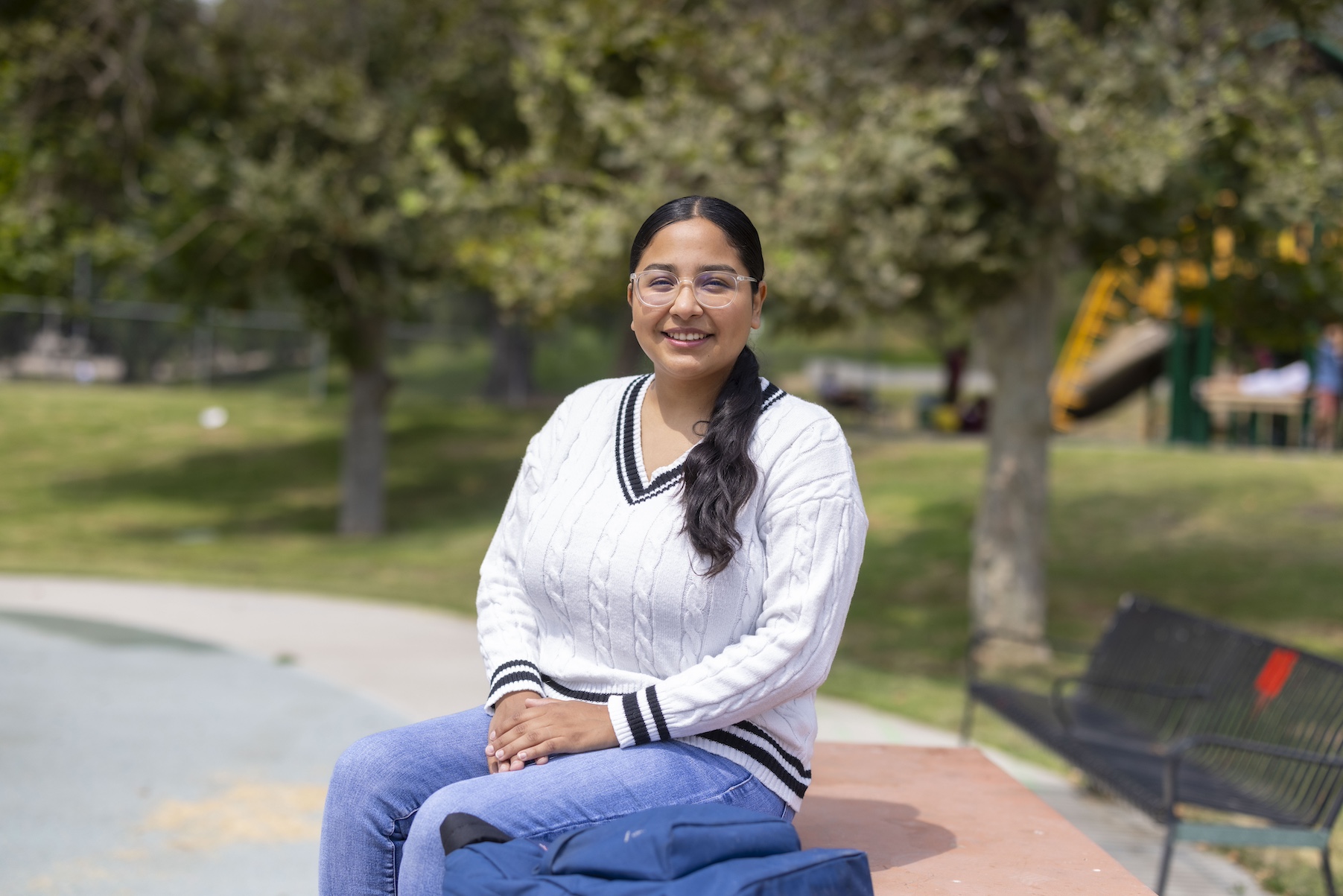 A woman poses for the camera while sitting on an outside bench at a park.