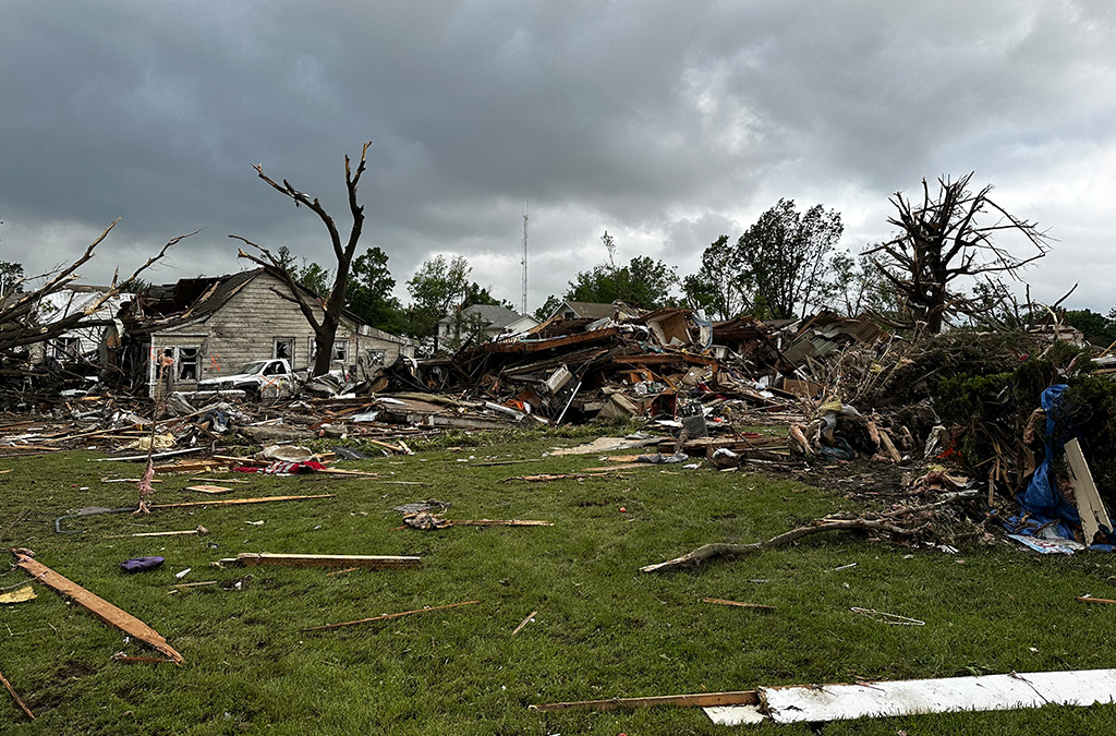 A house is destroyed by a tornado in Iowa, leaving only rubble and wooden planks on a grassy lawn. 