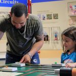 A father and daughter play together at a toy mechanical station at the traveling toy exhibit.