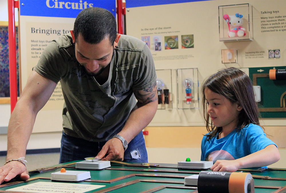 A father and daughter play together at a toy mechanical station at the traveling toy exhibit.